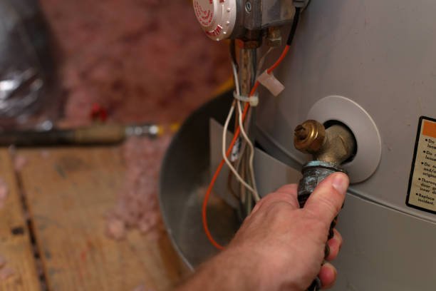 Hand attaches hose to water heater drain to perform maintenance