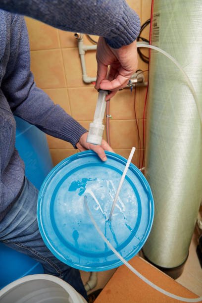 plumber hands are holding a round lid; in his right hand he is holding the suction filter of the osmosis water purification system.