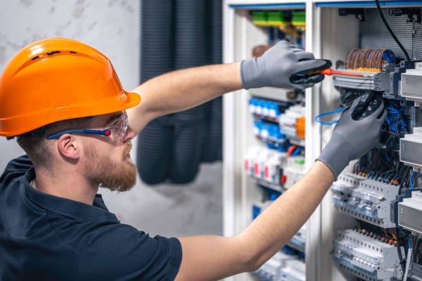 A male electrician works in a switchboard with an electrical connecting cable.